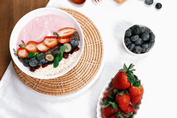 Presented by fruits putting yogurt toppings with strawberry, berry, oats, raisins and chia seed decorated by peppermint in white blow. Pink background. Set of healthy dairy product choice. Pecuniary.