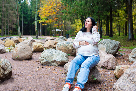 42 year old pregnant woman sitting on stones in autumn park. Pregnancy after 40, nature walks during pregnancy.