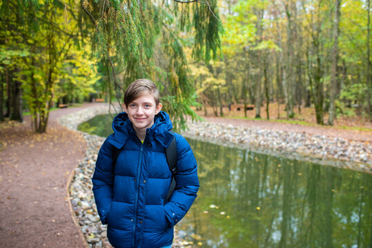 A 12 year old boy in a blue jacket walks along a cascade of ponds in Borovsky Park in autumn.