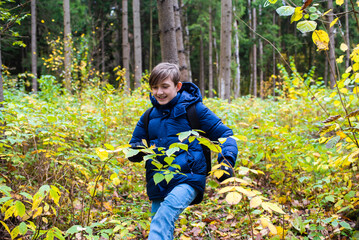 teenage boy in blue jacket walking in autumn forest or park