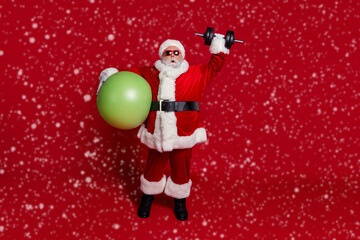 Photo of crazy old man hold fit ball lift heavy x-mas weights wear santa hat costume isolated red...