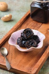 Green walnut jam in a pink bowl on a wooden tray on a green concrete background. Exotic sweets, recipes from around the world.