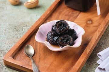 Green walnut jam in a pink bowl on a wooden tray on a green concrete background. Exotic sweets, recipes from around the world.