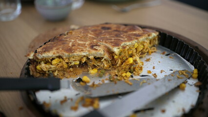 Partially eaten homemade savory pie with a golden crust, showcasing the delicious filling of chicken, corn, and vegetables, on a casual dining table in a cozy home environment