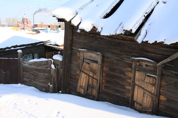 An old wooden house with a snow-covered roof stands weathered and worn