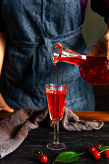 A woman's hand pours cherry liqueur into a glass. Homemade cherry liqueur