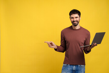 Successful Latin man holding laptop, pointing finger on copy space, isolated on yellow background