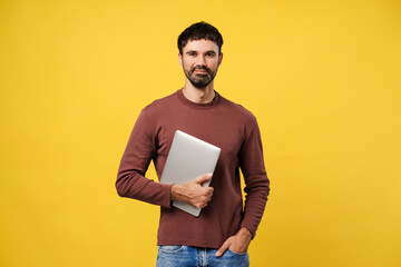 Fototapeta premium Success, confident man holding laptop, looking at camera standing isolated on yellow background