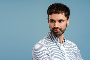 Attractive, confident man wearing blue shirt looking away standing isolated on blue background