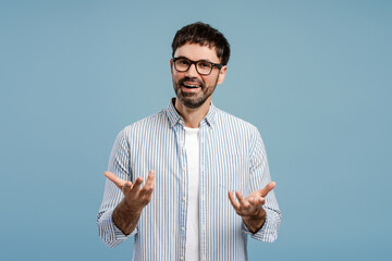 Handsome bearded man, wearing stylish eyeglasses gesturing something explaining looking at camera
