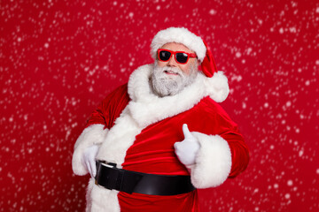 Portrait of attractive cheerful Santa showing thumbup advert ad recommend isolated over bright red color background