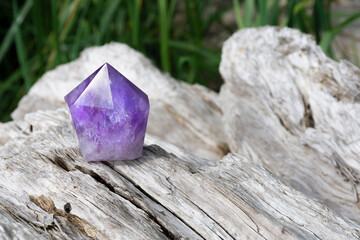An image of a sparkling amethyst crystal tower resting on a large piece of sun bleached driftwood. 