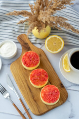 Top view of fresh mini fruit crumble cheesecakes on a wooden board with coffee, lemon and a decorative vase. Concept of dessert, gourmet food, and cozy breakfast. High quality photo 