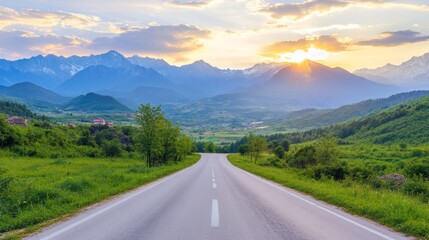 Fototapeta premium Asphalt Road Leading Through Green Meadow Towards Majestic Mountains. Summer Landscape At Sunset.
