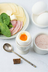 Boiled egg in a stand, pink Himalayan salt, ham, cheese, bread. Light breakfast, diet, nutrition