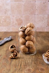 Walnuts in shell in glass jar on brown wooden background.