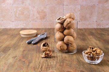 Walnuts in shell in glass jar on brown wooden background.