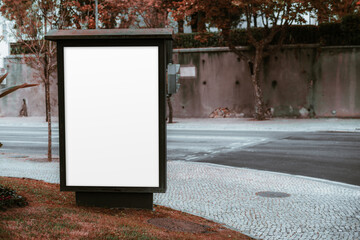 A blank urban billboard mockup set on a pedestrian walkway during autumn. The street and trees in...