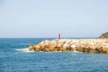 A breakwater made of white concrete cubes and a leading sign at the entrance to the port of Puerto de Vega. In Asturias, Spain.