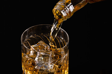 Glass of whiskey with ice cubes  on black background. As whiskey is poured from the bottle into the glass	