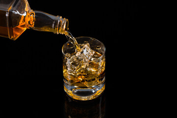 Glass of whiskey with ice cubes  on black background. As whiskey is poured from the bottle into the glass	