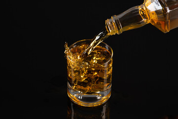 Glass of whiskey with ice cubes  on black background. As whiskey is poured from the bottle into the glass	