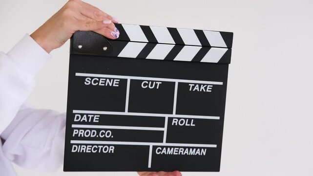 Film director in a white sweater is clapping a movie slate on a white background