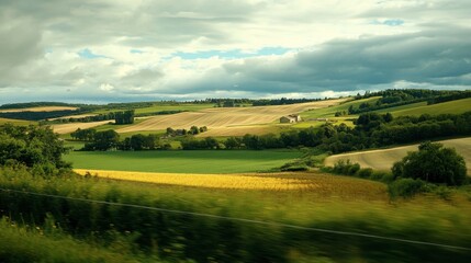 Obraz premium A scenic countryside landscape seen through the window of a train, with rolling hills and farms passing by.