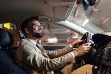 Young businessman searching for parking spot in underground garage. Driving around in his car.