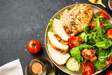 Healthy food. Green salad with grilled chicken meat at black table. Top view.
