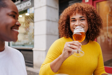 Trans woman drinking a craft beer with her friend and smiling to the camera.