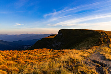 the last rays of the sun illuminate the yellow grass on the mountain ridge
