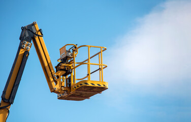 A bright yellow lift stretches towards the sky during a clear day, ready for workers to reach great heights