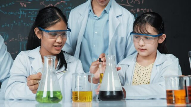 Smart teacher support and look after young diverse children doing experiment together. high school student with mixed races inspect biochemical liquid on table with microscope on table. Edification