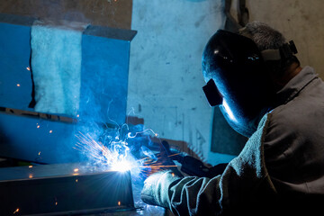 A worker performing welding in a dimly lit boiler room with sparks flying and protective gear on for safety