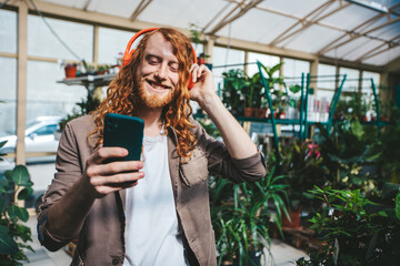 Red haired florist happily listens to music in a busy greenhouse, tending to plants with a smile