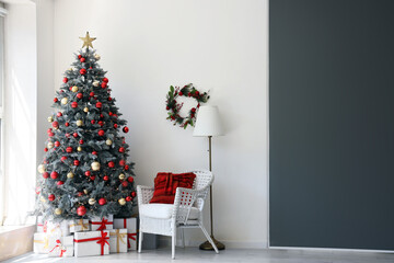 Gift boxes under Christmas tree and white armchair in festive room