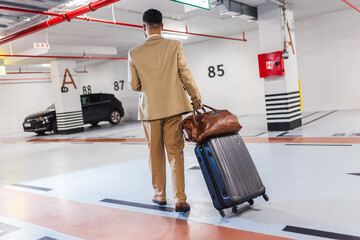 Backview of modern business man walking through parking lot with luggage. Going for a business trip.
