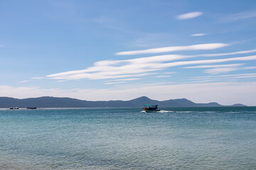 Serene coastal scene with clear blue sky and calm turquoise waters in Rach Vem, Phu Quoc island, Vietnam, South East Asia. Small boat is visible moving across the sea. Shoreline with distant hills