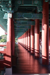 Sunlight illuminating red pillars creating a repeating geometric pattern leading towards a lush green garden