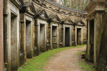 Gravel path is winding through old stone mausoleums with faded inscriptions in Highgate cemetery
