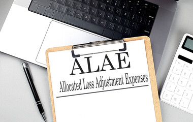  ALAE acronym meaning allocated loss adjustment expenses on clipboard with laptop, calculator, and...