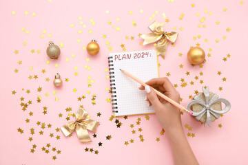 Woman writing PLAN 2024 in notebook and Christmas decor on pink background