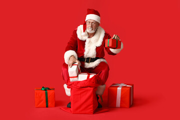 Santa Claus with bag full of gift boxes sitting on red background