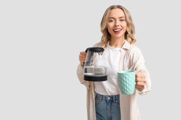 Beautiful young woman with modern electric kettle and cup on white background