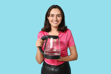 Beautiful young woman with modern electric kettle on blue background