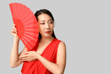 Beautiful young Asian woman with fan on grey background. Chinese New Year celebration