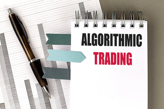  Algorithmic trading text on notepad with pen, financial charts, and bookmarks on gray desk