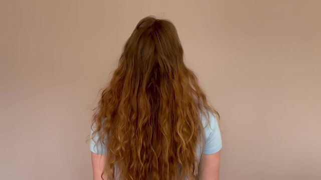 view from behind, unrecognizable woman, shows long, thick and curly hair, red or light brown
