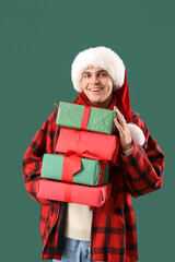 Happy young man in Santa hat with Christmas gift on green background